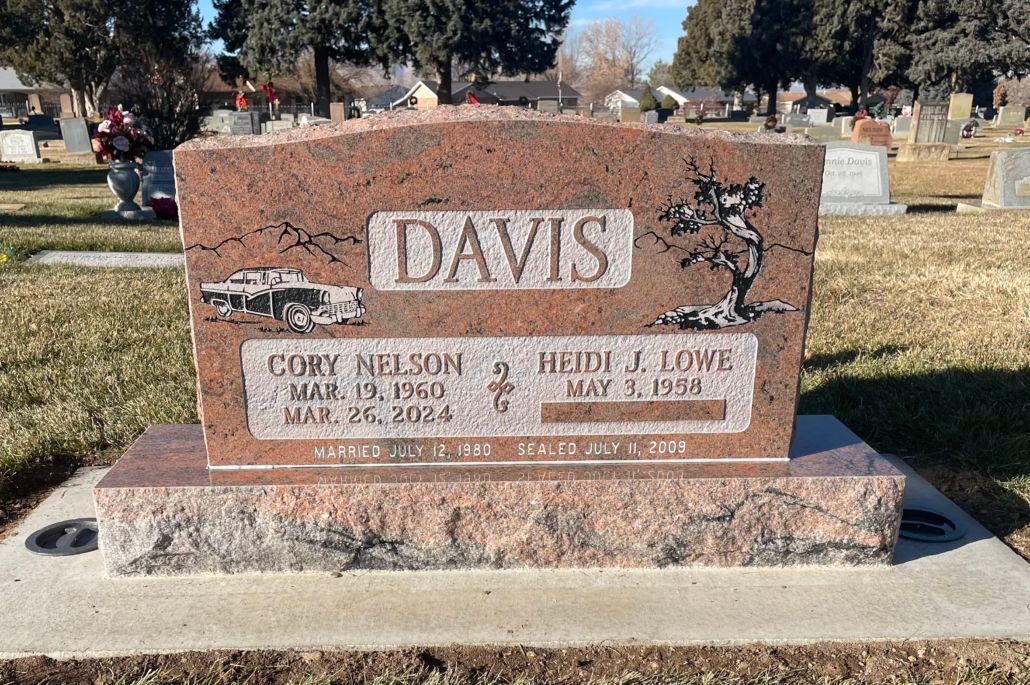 Red granite headstone in a cemetery for the Davis family; a car and tree are etched on the stone.
