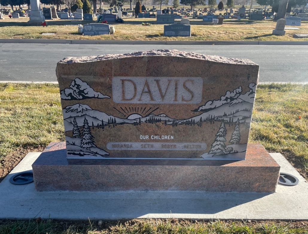 Headstone engraved with DAVIS, a mountain scene, and names, standing in a cemetery.