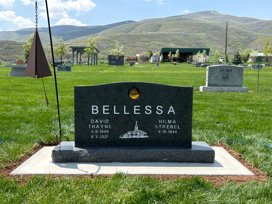 Headstone with the name BELLESSA in a cemetery, with a mountain backdrop.