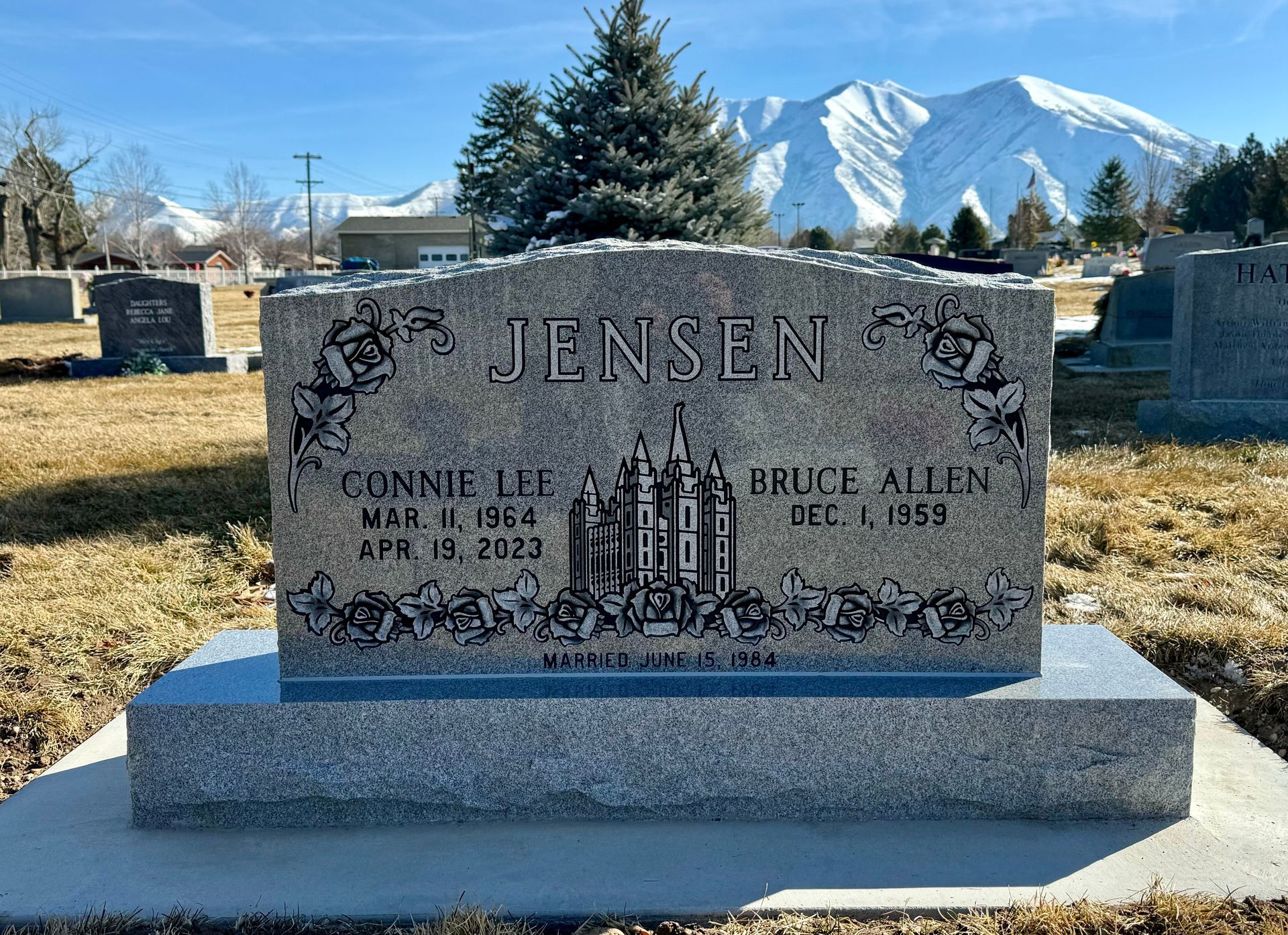 Headstone for Connie Lee and Bruce Allen Jensen in a cemetery with mountains in the background.