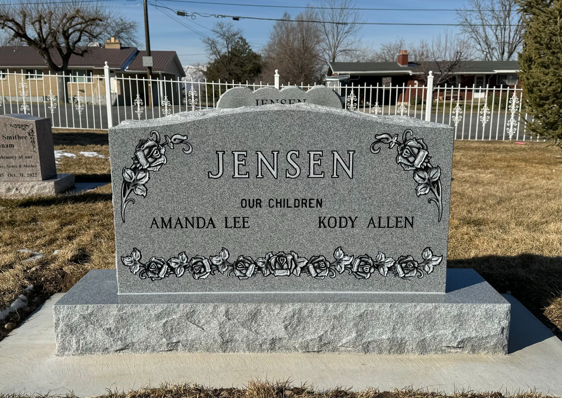 Gray granite headstone with Jensen and names of Amanda Lee and Kody Allen; in a cemetery.