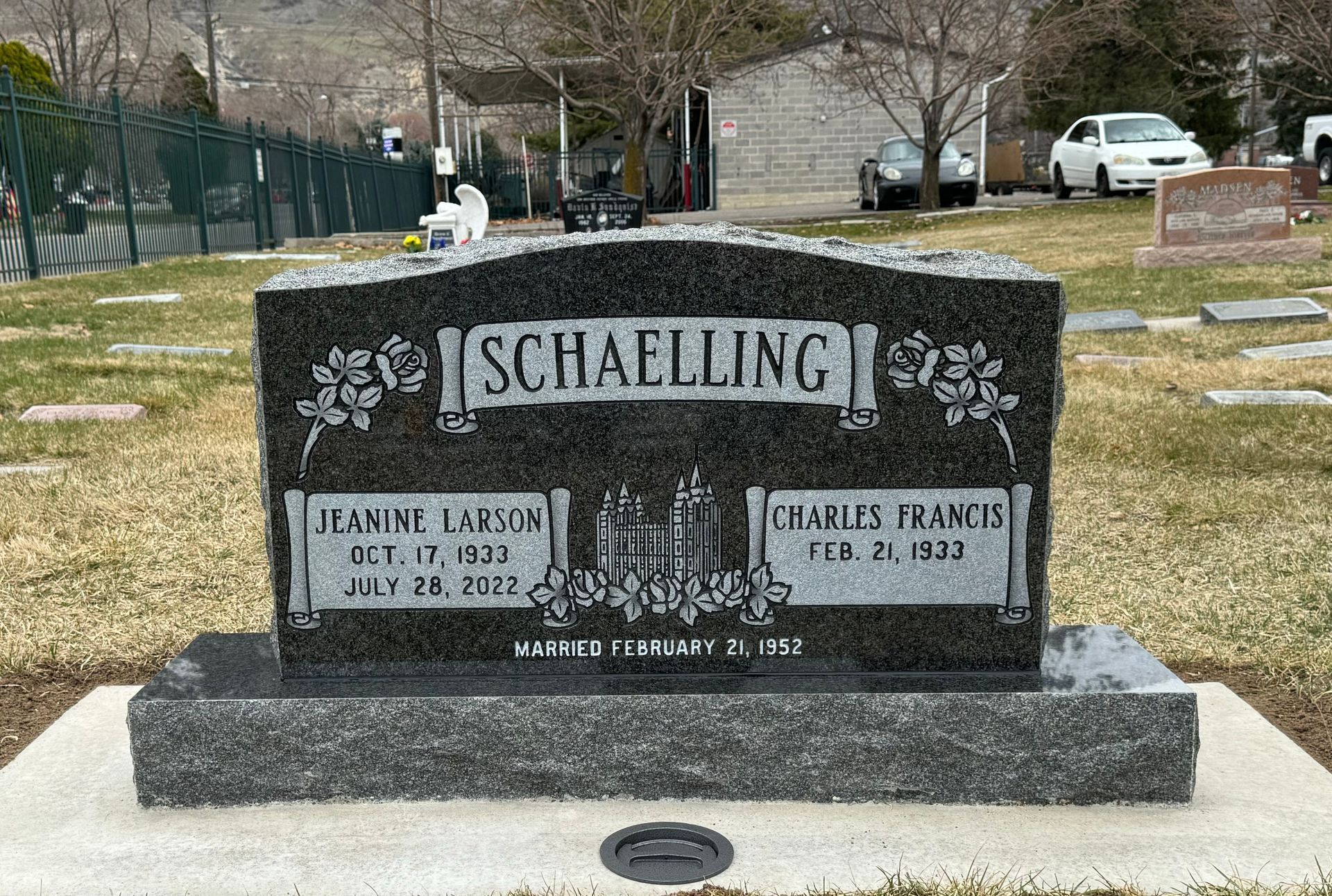 Headstone for Jeanine and Charles Schaelling in a cemetery. Black granite with white text and floral design.