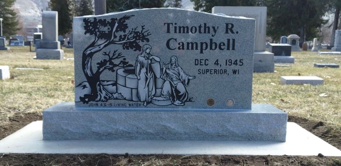 Gray headstone with black etched design of figures and tree; reads Timothy R. Campbell DEC 4, 1945, Superior, MI.