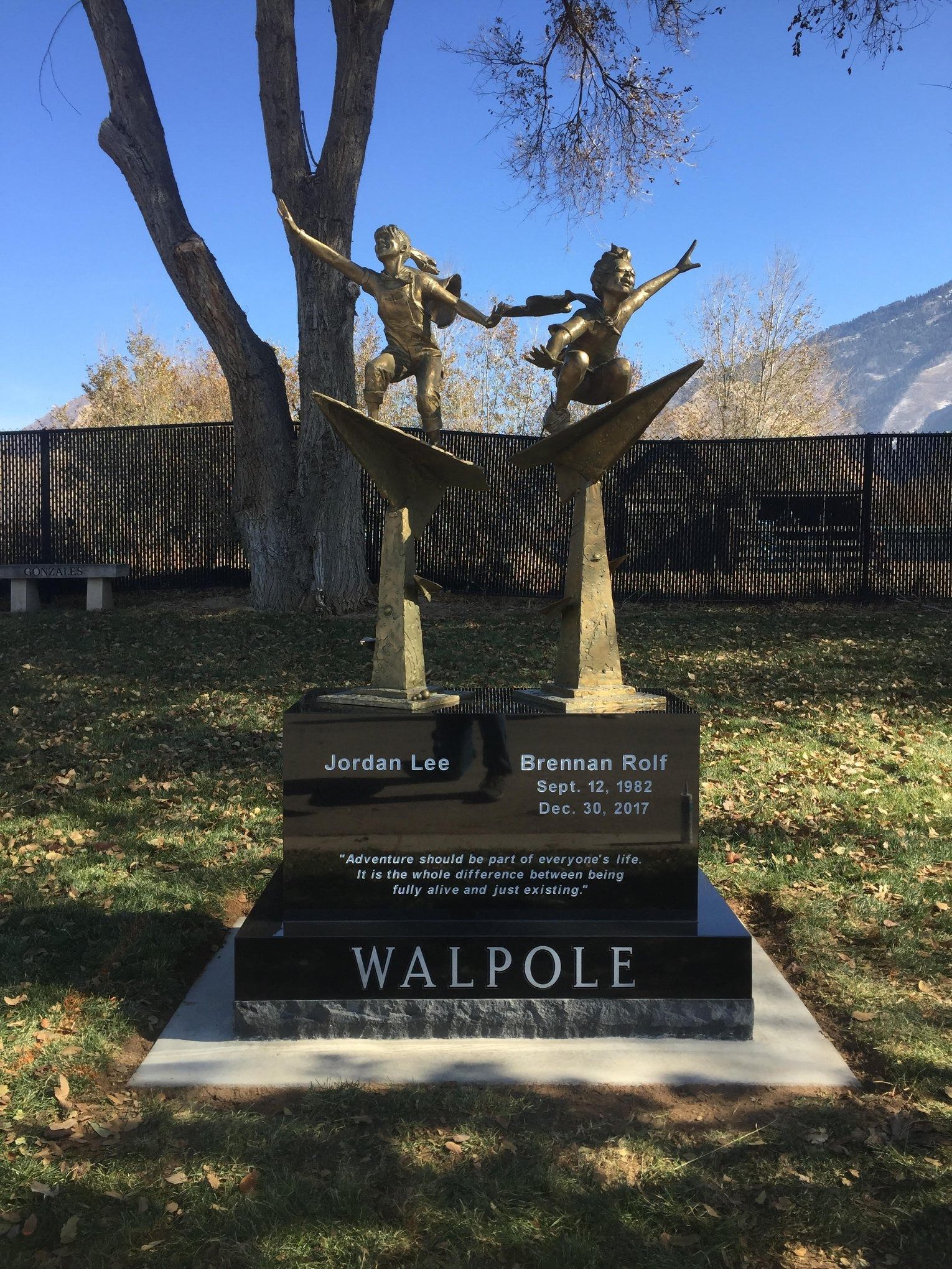 Bronze statue of two children dancing atop a black marble memorial. 