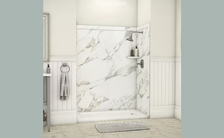 Marble-look shower stall in a bathroom, with a showerhead, shelves, and a gray bathmat on the floor.