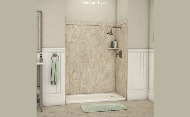 Shower stall with beige walls, shower head, and shelf. A rug and towel hang on the wall.