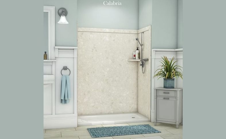 Bathroom with a light-colored shower, blue rug, and vanity. Light blue walls and white trim. A potted plant sits near a small cabinet.