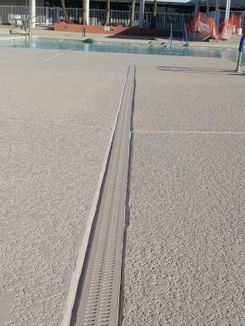 A drain on the side of a concrete floor next to a swimming pool.