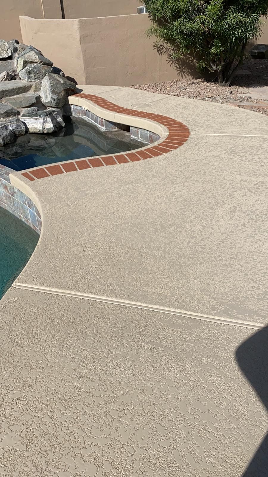 A concrete walkway leading to a pool with a brick border.