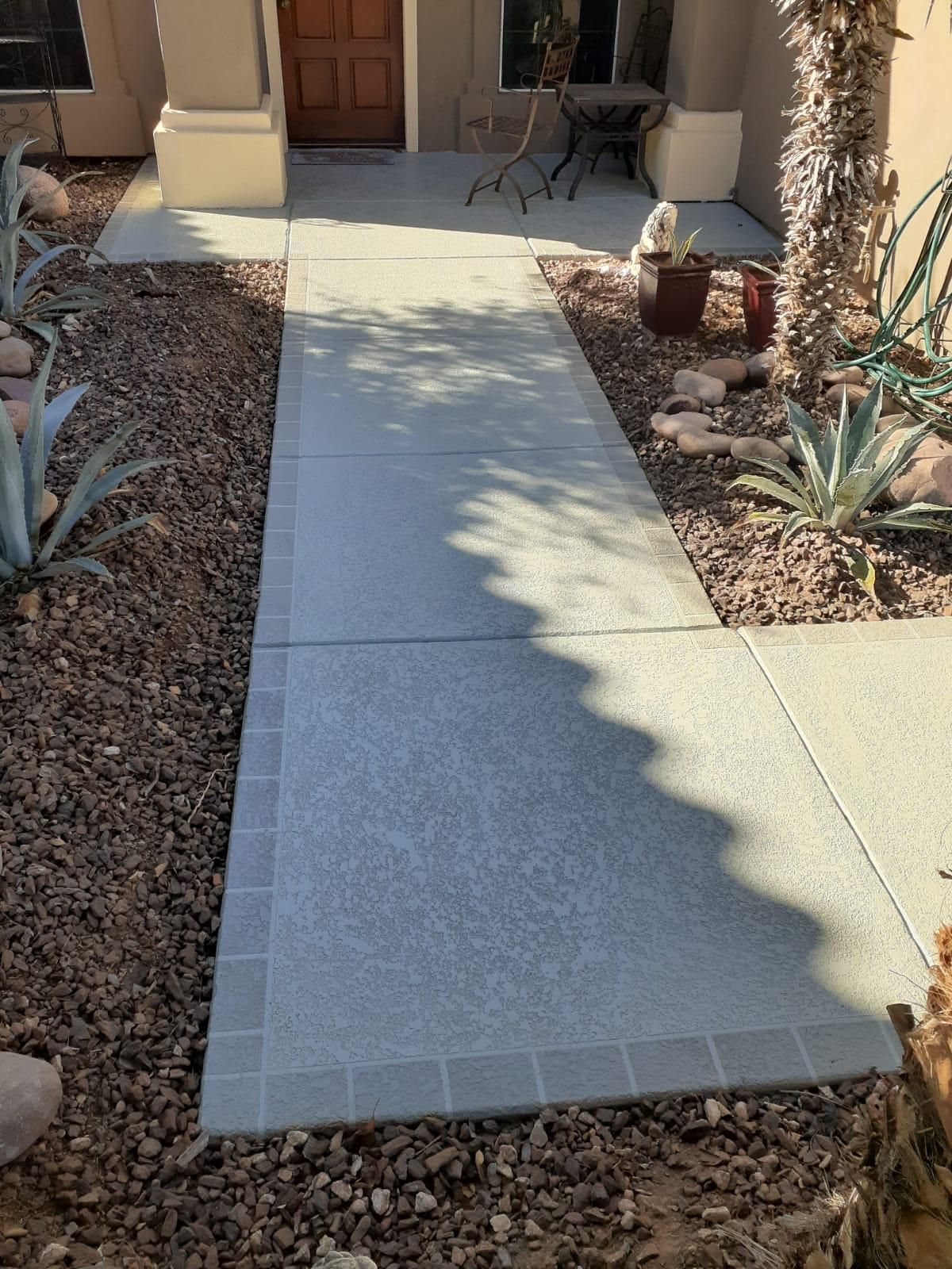 A concrete walkway leading to a house with a table and chairs