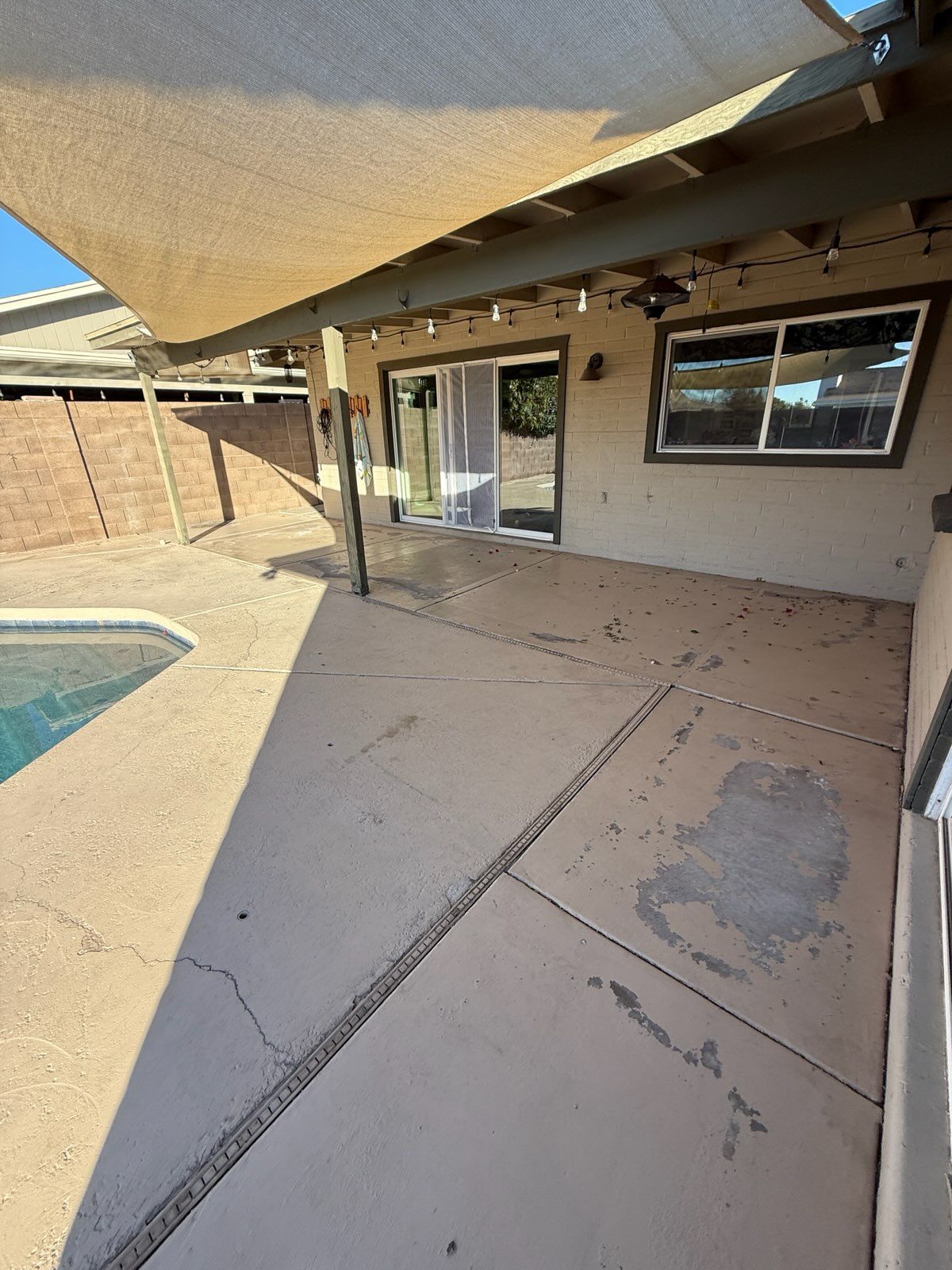A patio with a sliding glass door and a pool in the background.