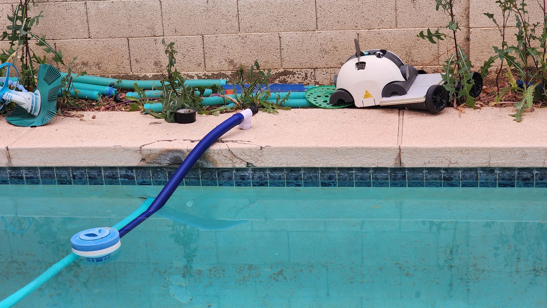 A robotic pool cleaner is sitting on the edge of a swimming pool.