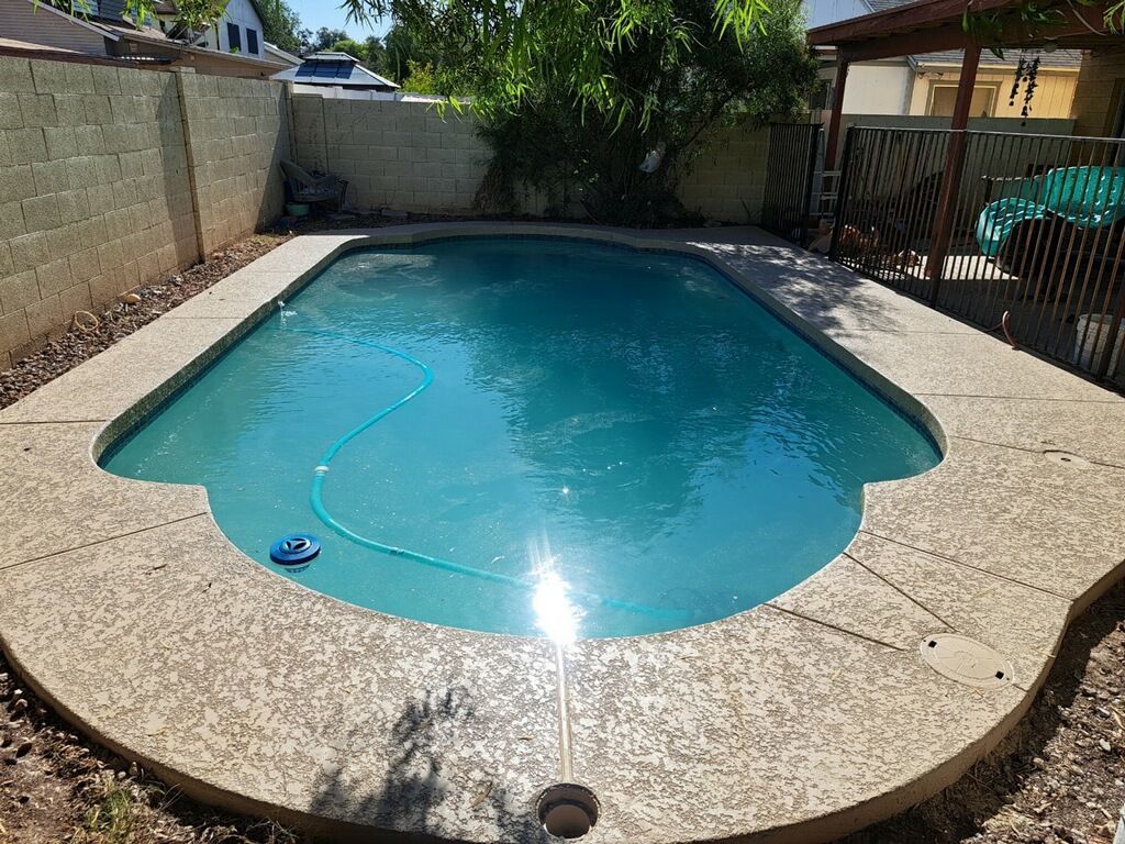 A large swimming pool in a backyard with a hose attached to it.
