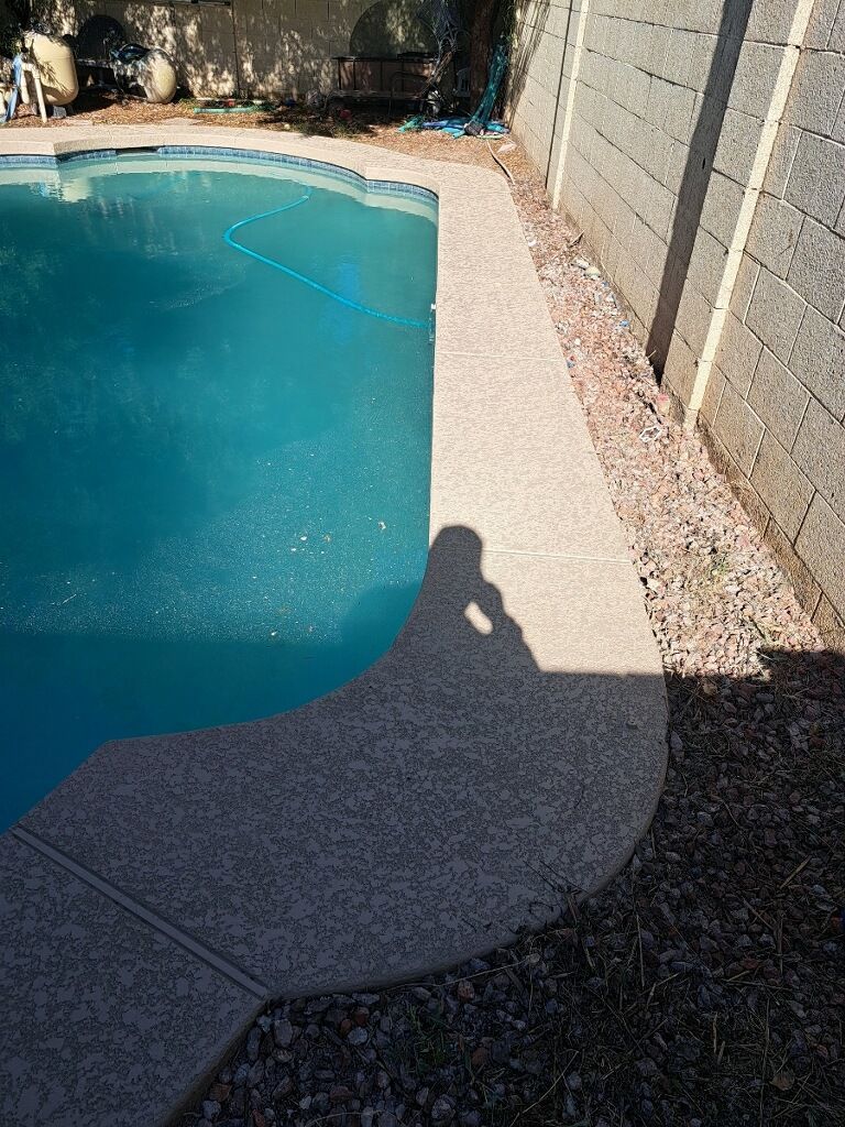A shadow of a person is cast on the side of a swimming pool.