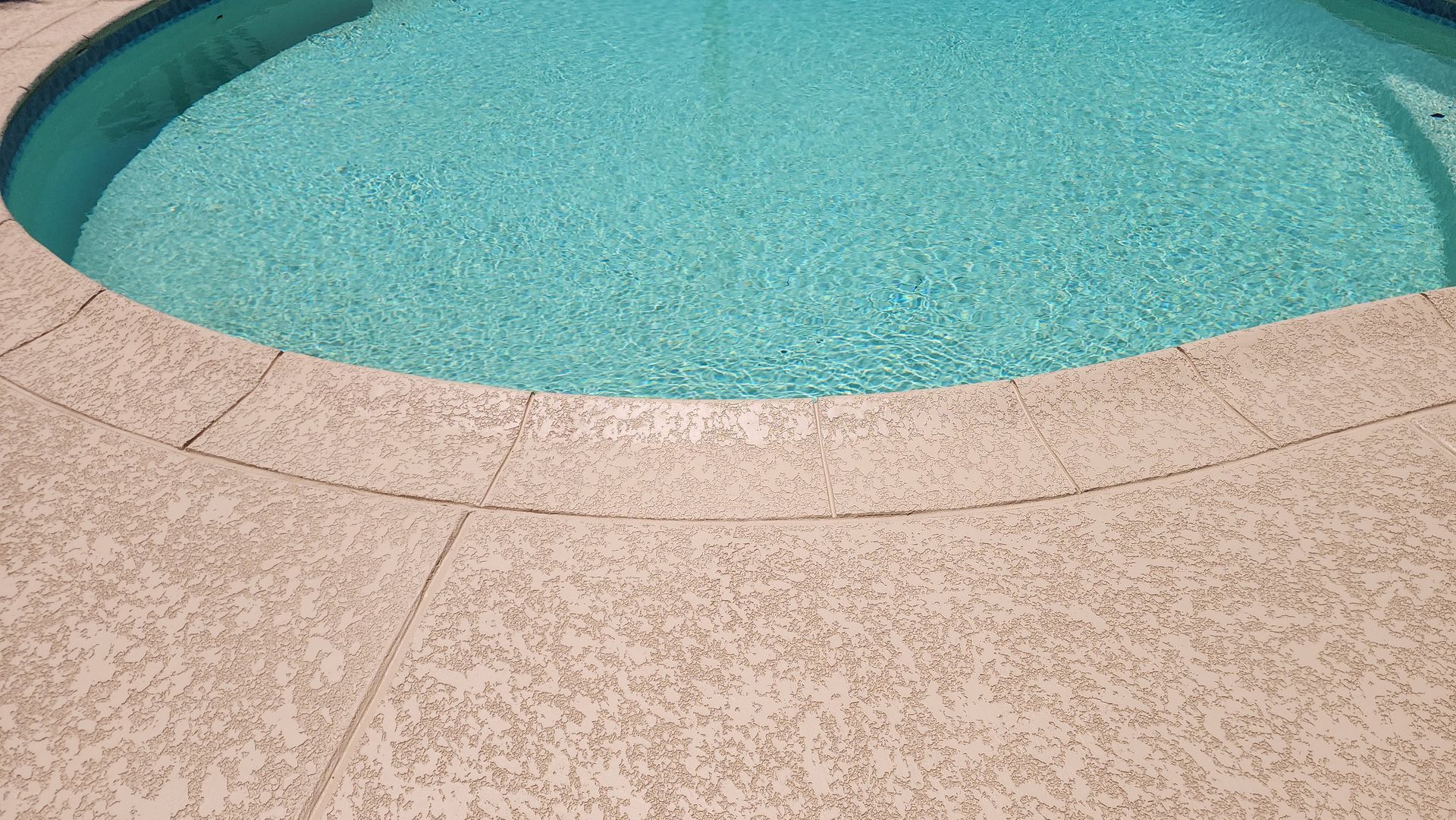 A swimming pool with turquoise water and a concrete deck surrounding it