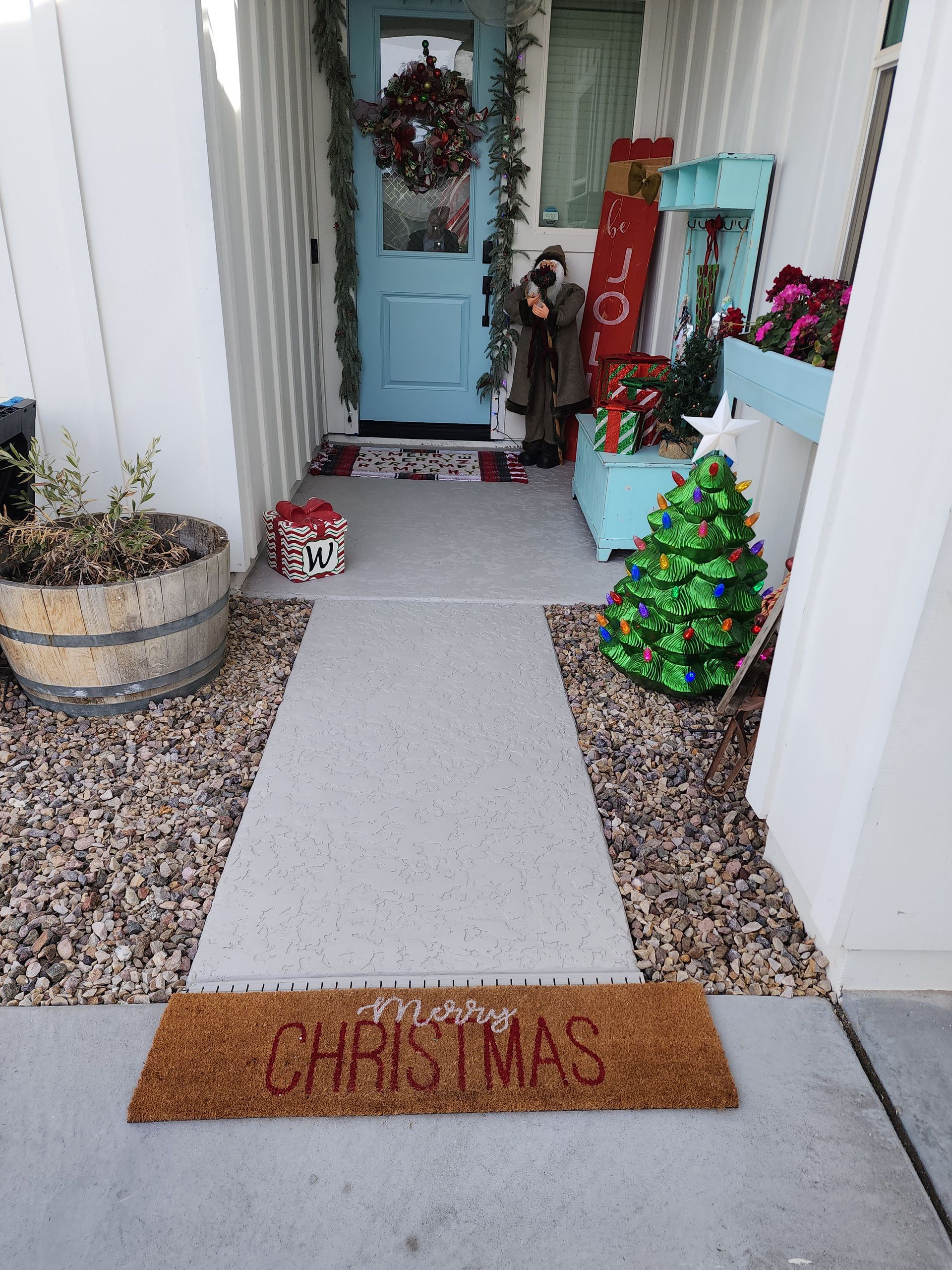 A Christmas welcome mat is on the sidewalk in front of a house