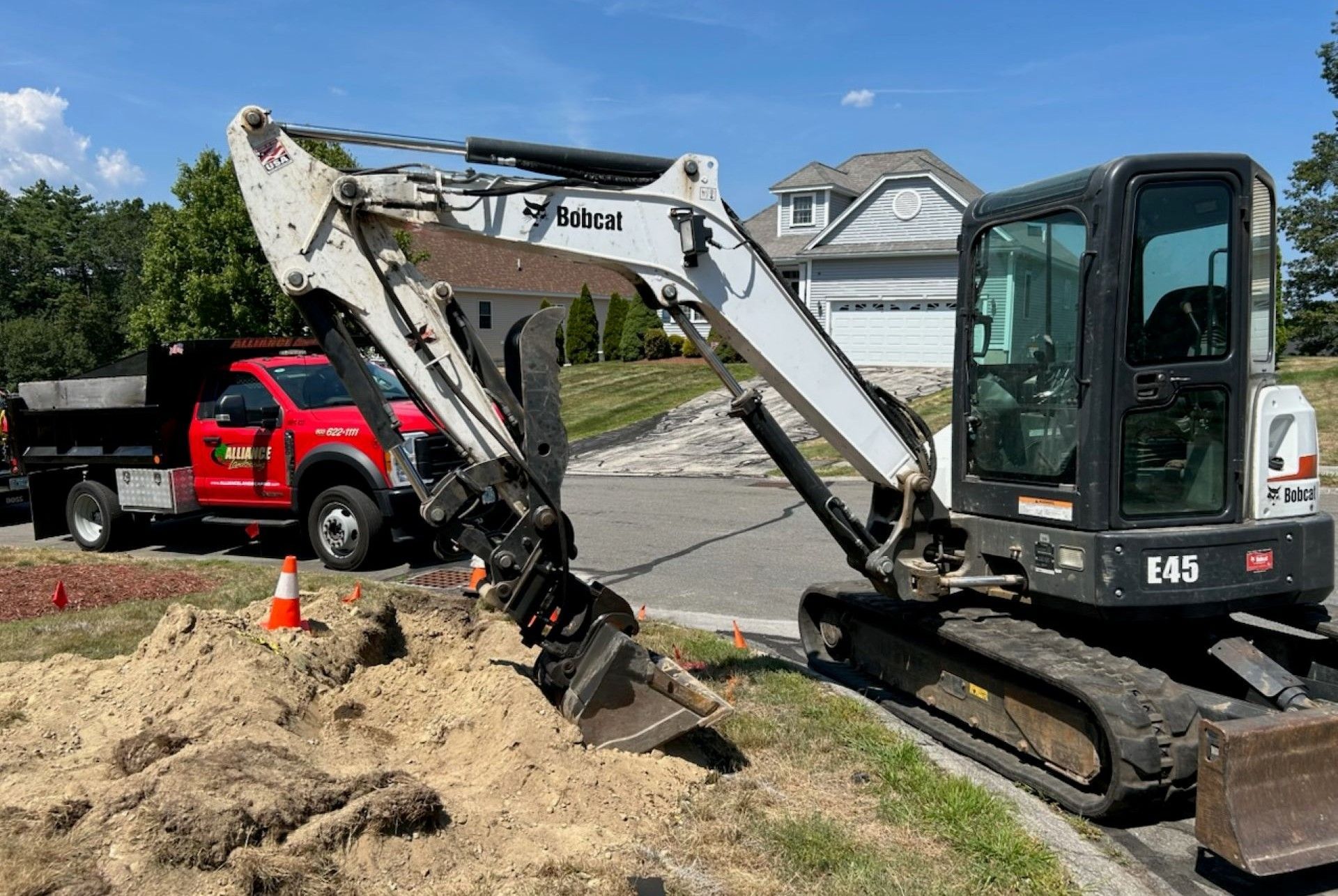 Bobcat E43 excavator digging near curb, red truck in background. Sunny day.