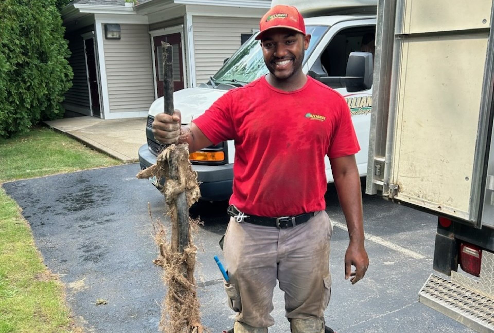 Plumber holding large clog outside, wearing red shirt, standing near truck.