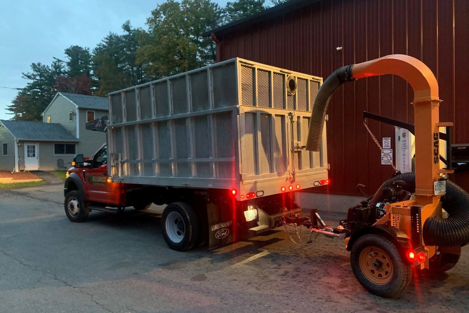 Orange truck with a leaf vacuum attached, next to a large metal bin.