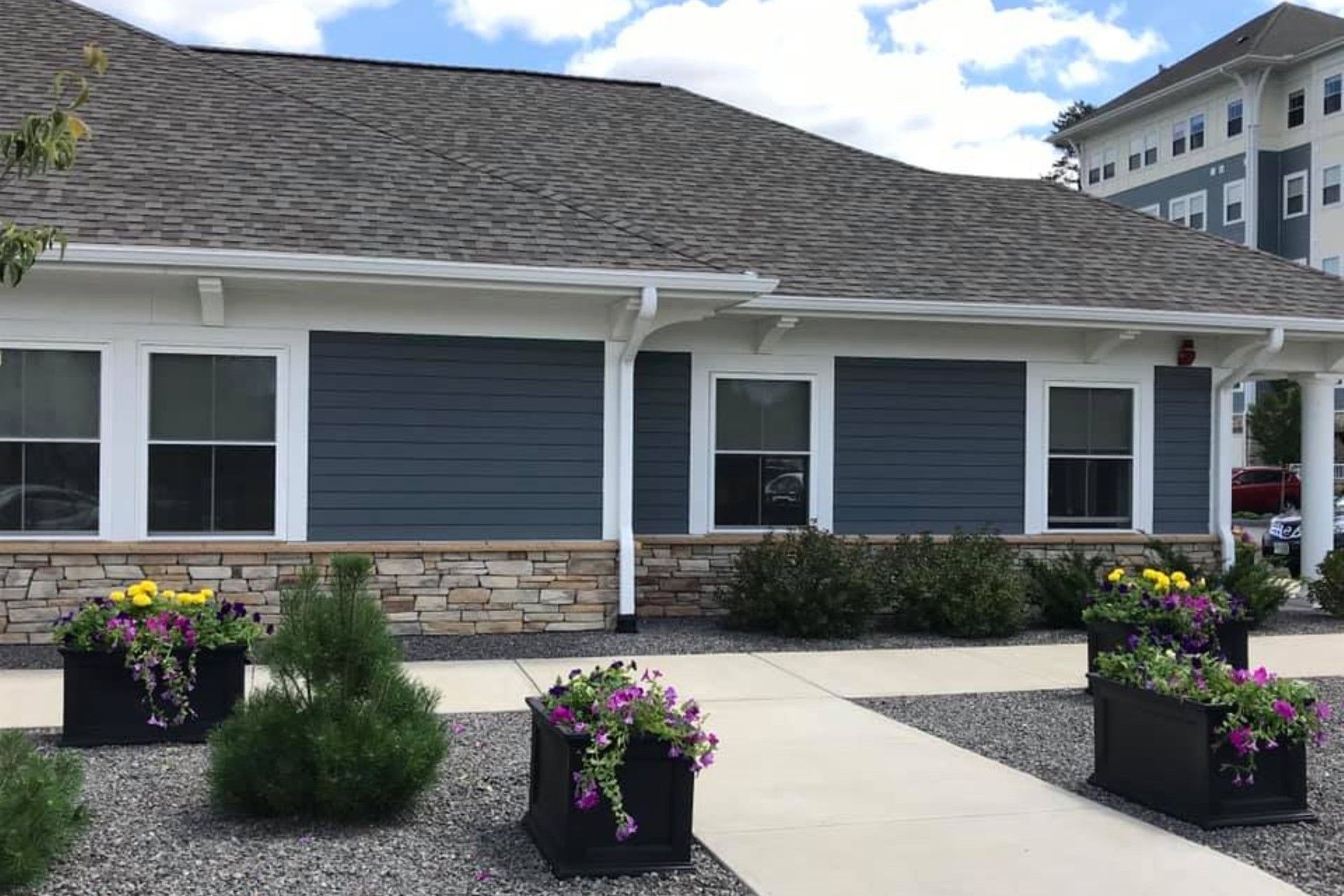 Low-rise building with blue siding, stone base, and flower boxes. Gray roof, white trim.