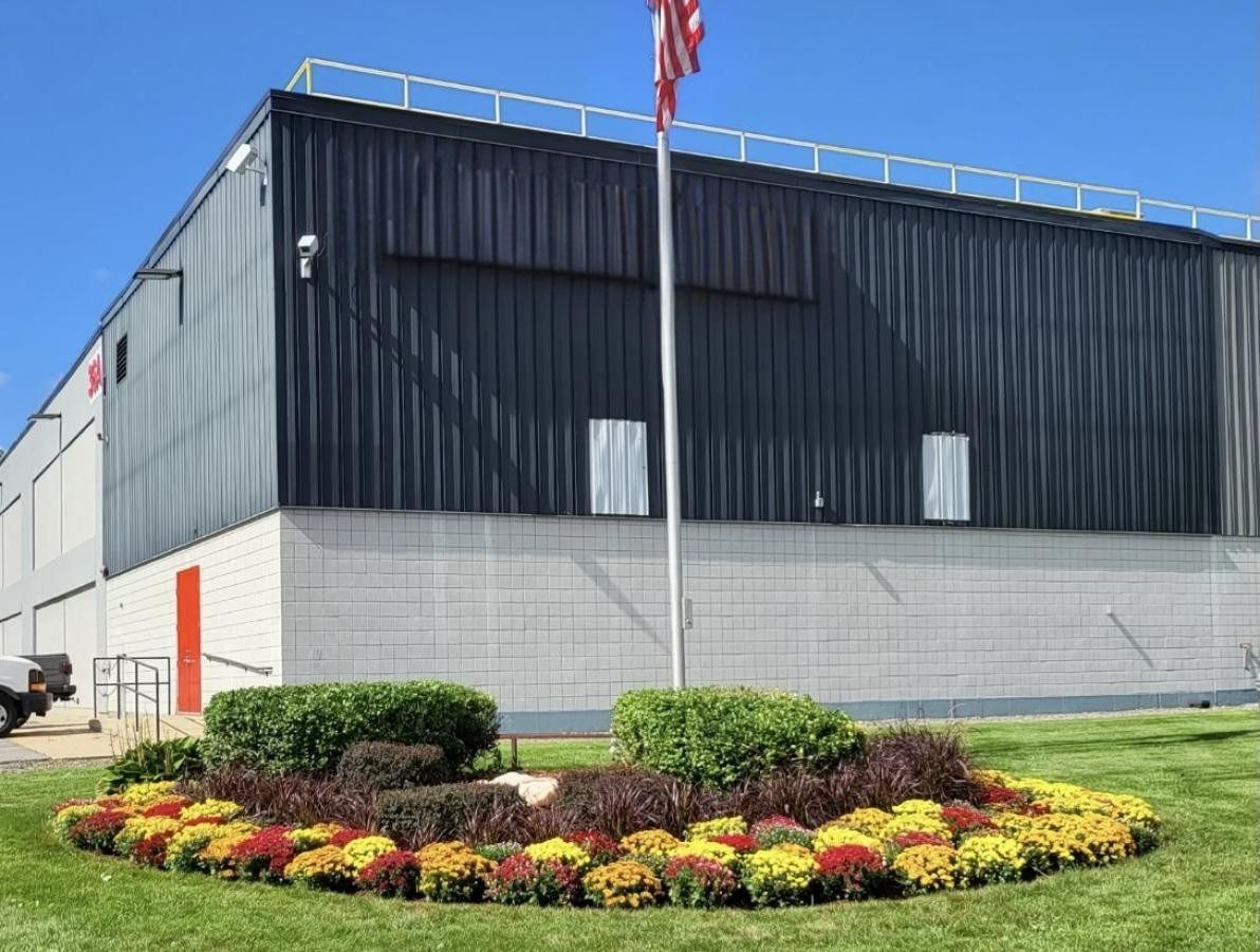 BAE Systems building with red sign, flag, and flowerbed.
