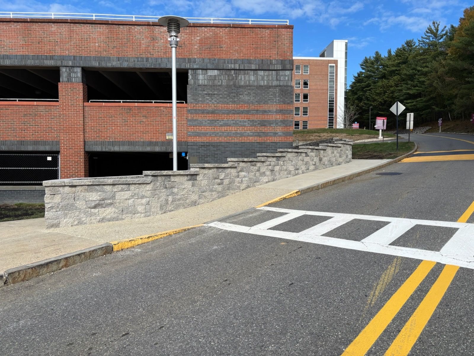 Brick parking garage and stone wall adjacent to a road with crosswalk and double yellow lines.