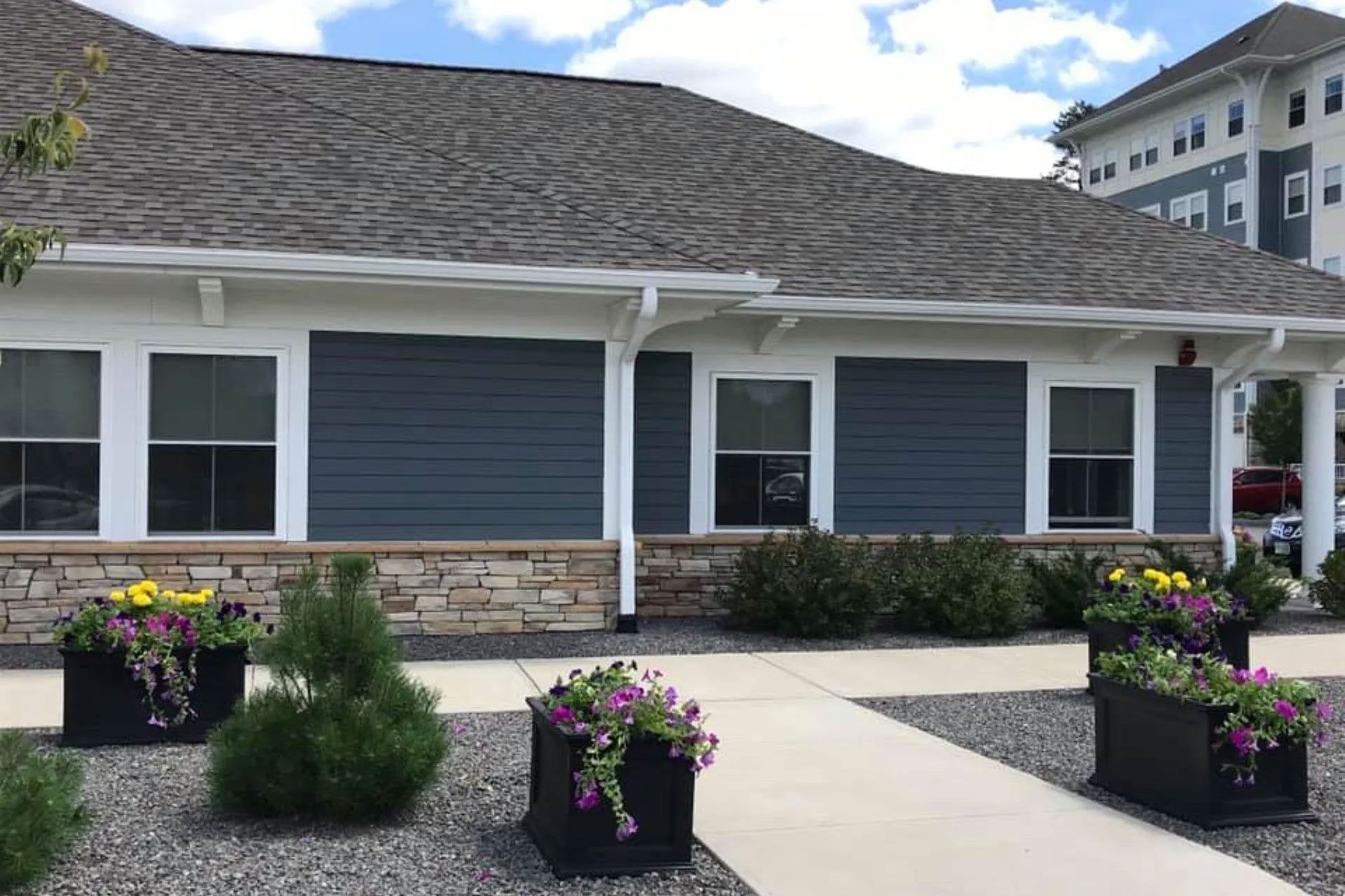 Low-rise building with blue siding, stone base, and flower boxes. Gray roof, white trim.
