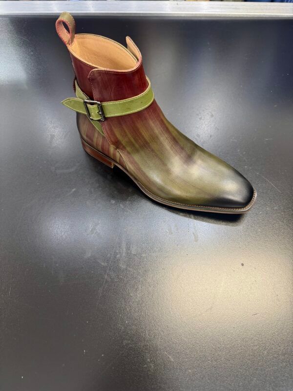 A pair of brown and green boots with a green buckle on a black surface.