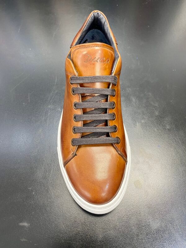 A pair of brown leather sneakers with brown laces on a black surface.