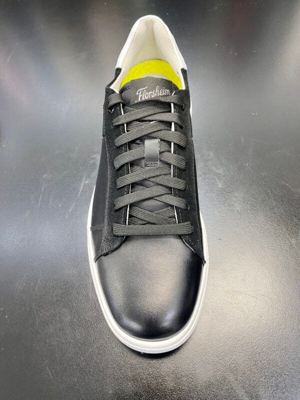A pair of black sneakers with white laces on a black surface.