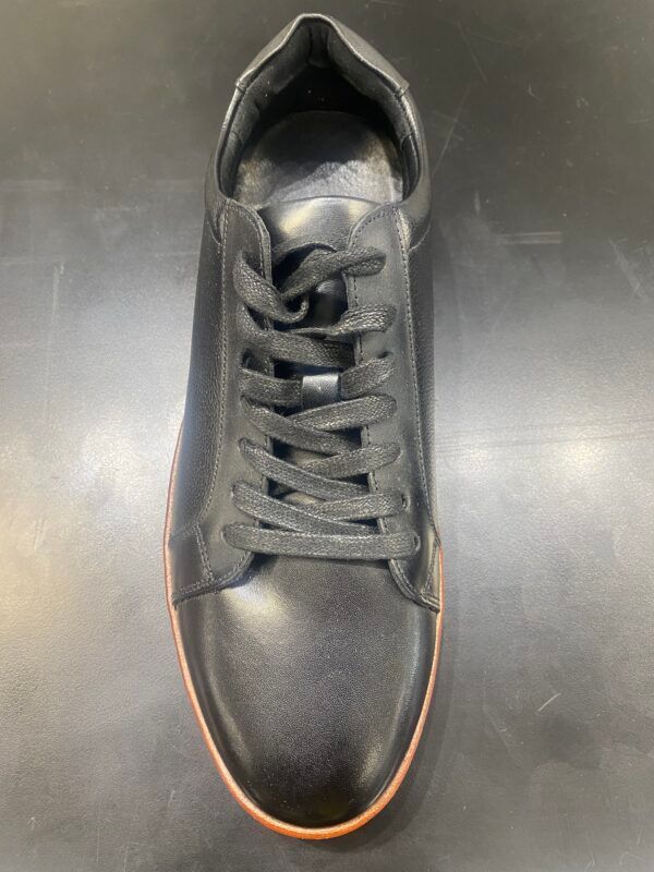 A pair of black sneakers with brown soles are sitting on a black surface.