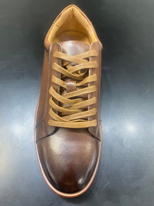 A pair of brown leather sneakers with tan laces on a black surface.