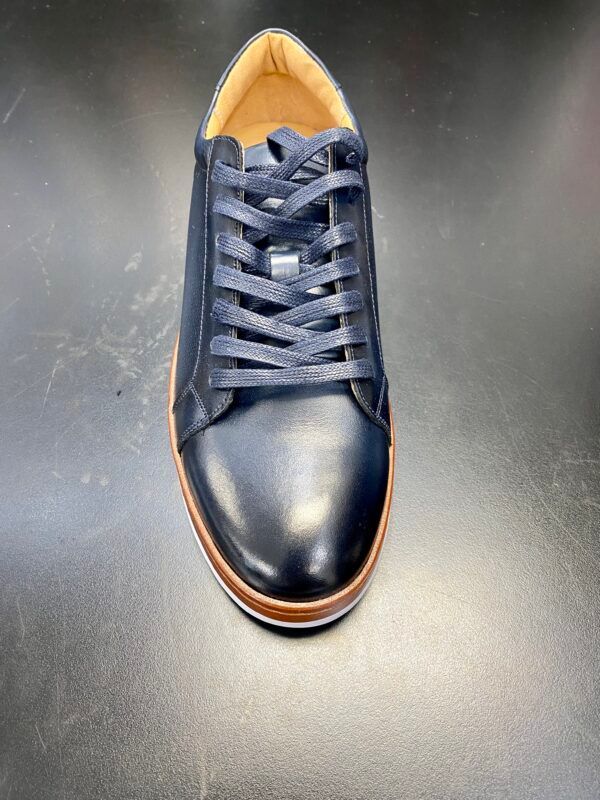 A pair of black leather sneakers with brown laces on a black surface.