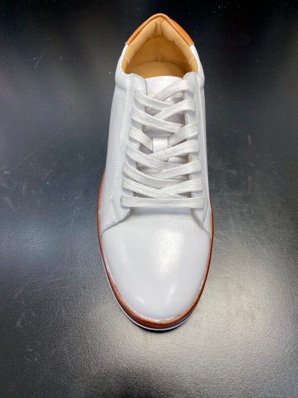 A pair of white sneakers with brown laces on a black surface.