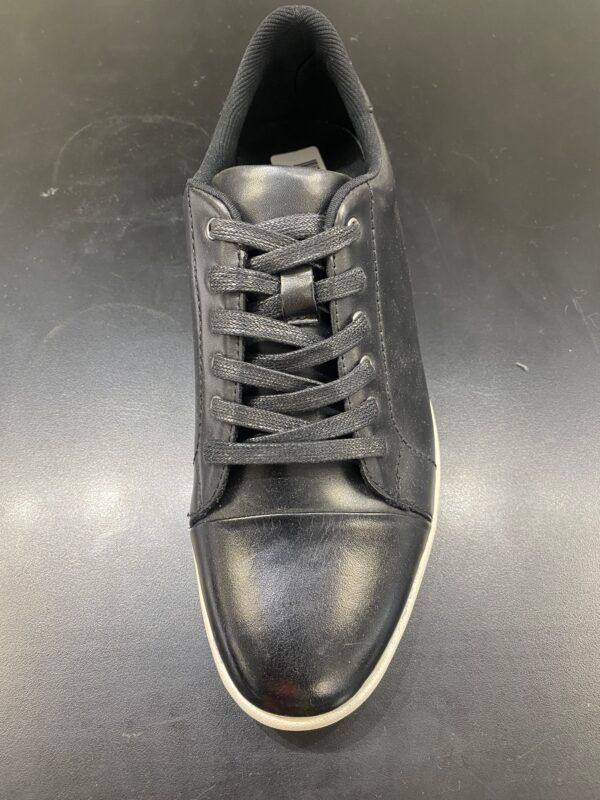 A pair of black sneakers with white laces on a black surface.