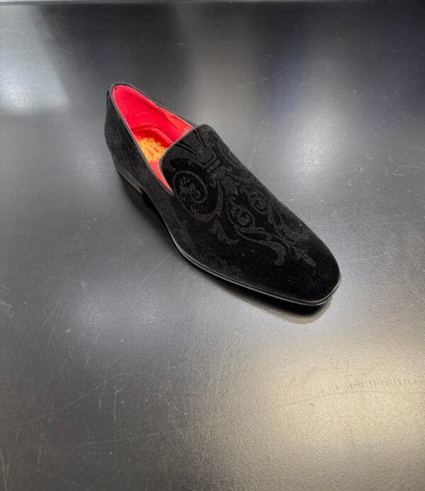 A black shoe with a red sole is sitting on a black surface.