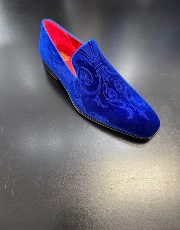 A pair of blue velvet loafers with red soles on a black surface.