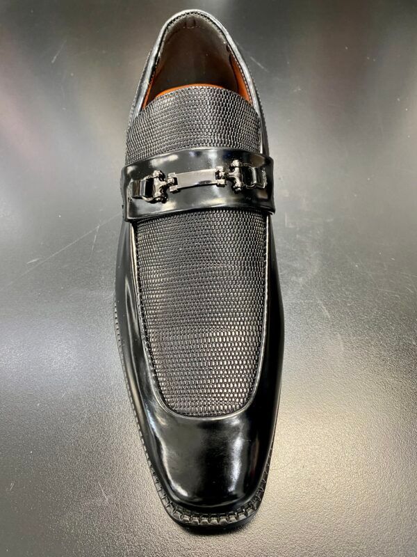 A pair of black loafers with a metal buckle on a black surface.