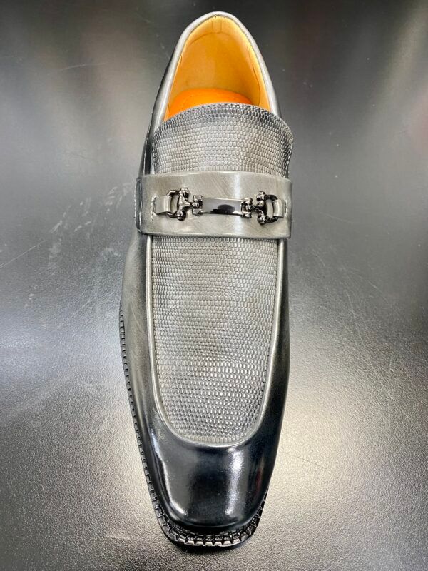 A pair of black loafers with a silver buckle on a black surface.
