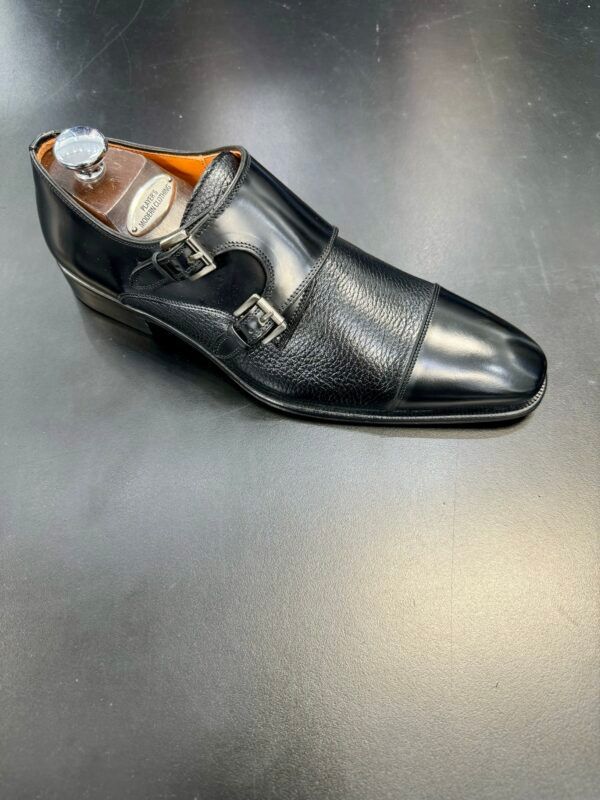 A pair of black double monk strap shoes on a black surface