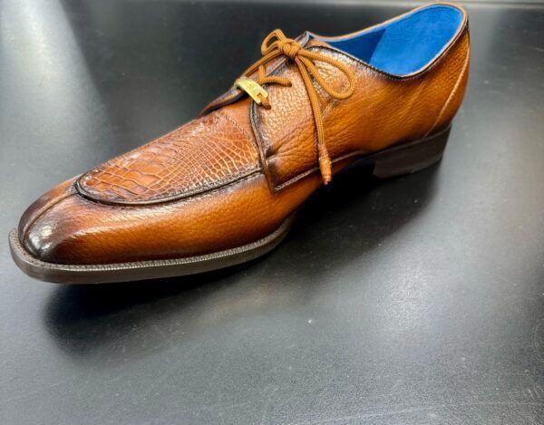 A brown shoe with a blue sole is on a black surface