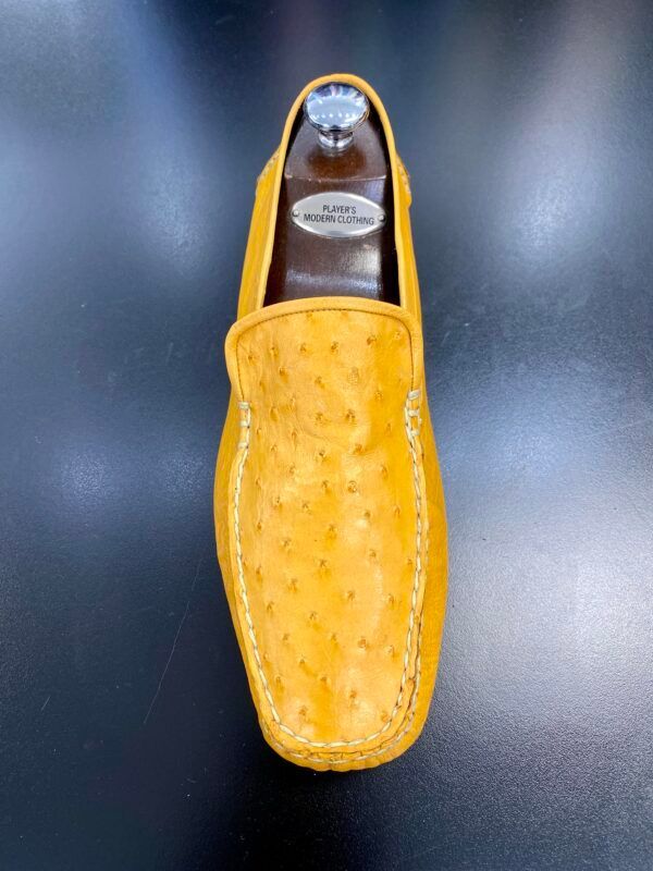 A pair of yellow ostrich leather loafers on a black surface.