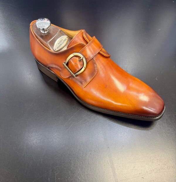 A brown shoe with a gold buckle is sitting on a black surface