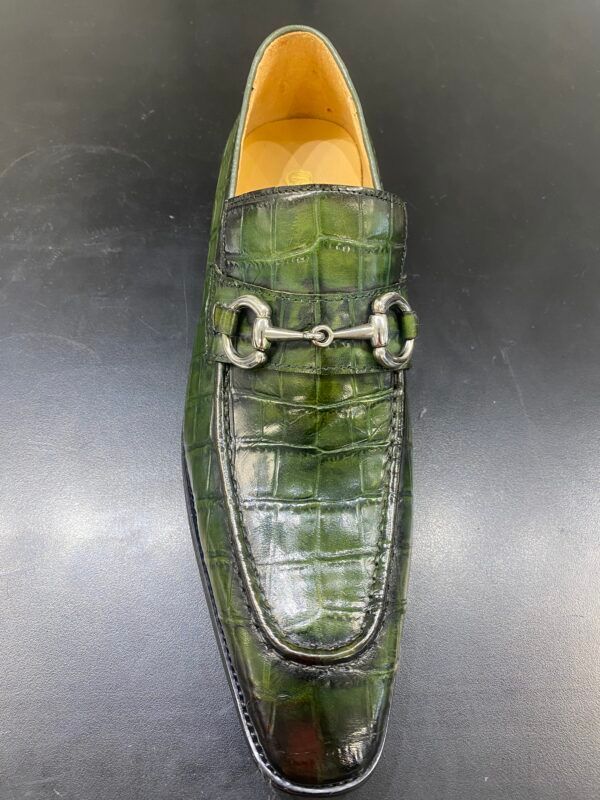 A pair of green shoes with a horse bit on a black surface.
