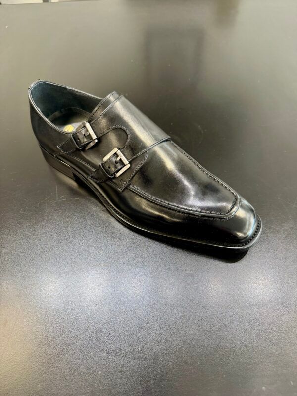 A pair of black double monk strap shoes are sitting on a black table.