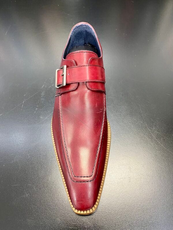 A pair of red leather shoes with a buckle on a black surface.
