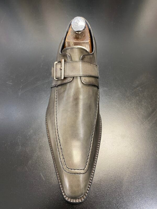 A pair of grey leather shoes with a buckle on a black surface.