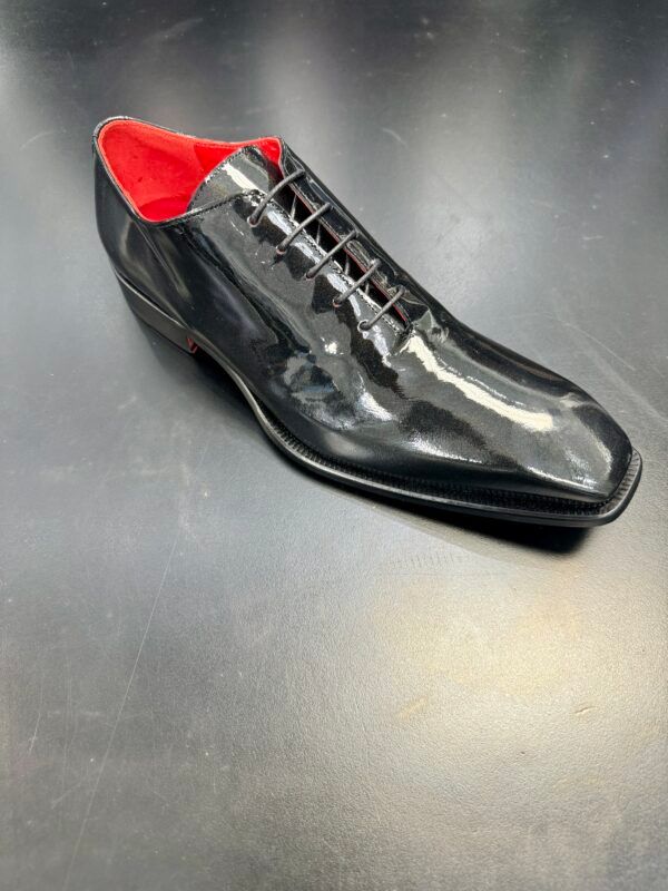 A black shoe with red laces is on a black surface