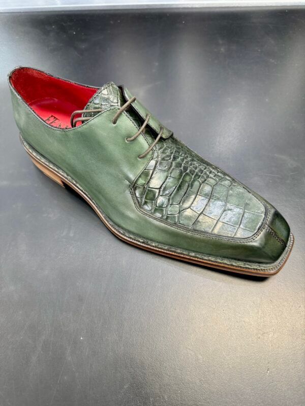 A green shoe with a red sole is sitting on a table.