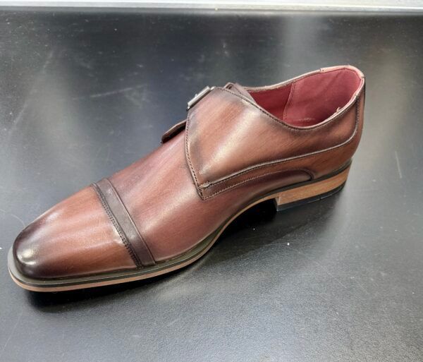 A brown shoe with a red sole is on a black surface
